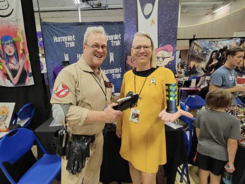 Sarah holding the Ghost F*cker candle from ST:TNG Sub Rosa next to a Ghostbuster at Fort Collins Comic Con 2024