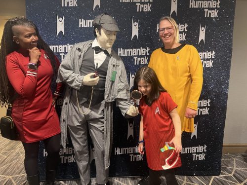 Sarah and Allie with Data cosplayer in Sherlock Holmes attire showing a young Trekkie a magnifying glass