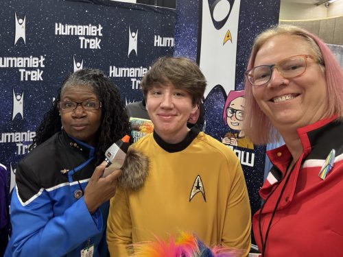 Sarah and Allie in Lower Decks uniforms with a convention goer wearing a TOS gold uniform with a brown tribble attached.